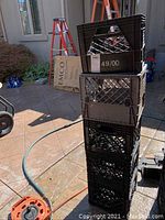 Stack of five plastic milk crates in black and grey with visible wear and numeric markings.