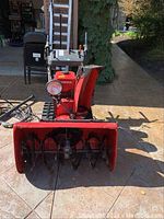 Front view showing red two-stage auger housing and serrated rubber tracks