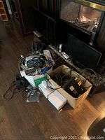 Photo showing three flat-screen monitors leaning against a fireplace, with two boxes in front filled with cables and electronic items.