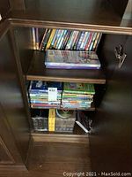 Photo showing cabinet with multiple shelves holding several stacks and rows of DVDs including boxed sets and standard DVD cases.