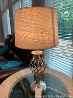 Single lamp lit, side view on round glass-topped table against window blinds