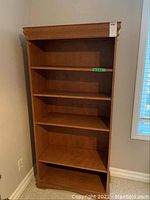 Front view of wood bookcase showing five shelves and decorative top and base trim.