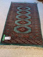 Full view of rectangular Pakistani area rug showing teal color with reddish-brown and black geometric patterns, fringe on one end