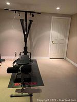 View of Bowflex home gym bench and tower mounted on rubber mat with logo