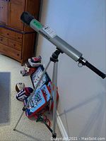 Silver Bushnell telescope mounted on aluminum tripod leaning against wall