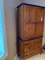 Front view of two-piece armoire showing upper cabinet doors and lower drawers against wall.