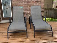 Front view of two gray mesh fabric adjustable back deck loungers with black metal frames sitting side by side on wood deck, showing overall condition and design.