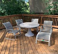 Group shot showing round pedestal table with three mesh fabric arm chairs, rocking chair and footrest on wooden deck.