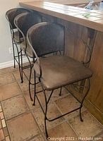 Three dark metal bar stools with curved backs and leather seats arranged at a tiled bar counter