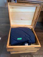 Open wooden box with dark-colored throw blanket inside on hardwood floor.