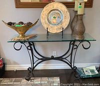 Front view of black wrought iron hall table with beveled glass top, showing decorative curves and wear.
