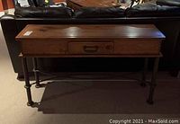Front view of table showing wood top, center drawer with metal handle, and wrought iron legs