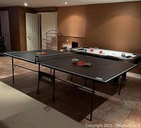 Full view of table set up in basement with paddles and balls on surface