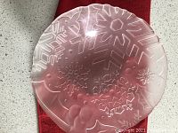 Translucent glass snowflake dish/bowl with etched snowflake shapes and rounded edges, placed on a red cloth surface.