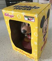 View of Kellogg's Walt Disney World Mickey Mouse bobble head in original packaging box, showing front and left side of the box and figure inside.