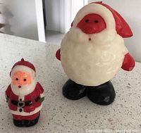 Two antique wax candle Santas, one smaller with red and white details and another larger with a round body and red face