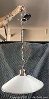 Photo of brand new hanging light fixture, showing glass shade and metal chain mount held by hand.
