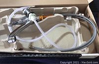 Moen kitchen sink faucet in packaging showing chrome body, attached hoses, and mounting hardware.