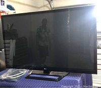 Front view of the 55-inch LG TV showing the screen and stand, placed on a blue padded cloth.