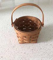 Photo of small round basket with swing handle, showing woven wood pattern and natural finish.