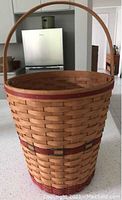 Woven wooden basket with single large handle and reddish accents near rim and base.