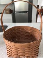 Photo showing the Round Gathering basket with tall curved handle and square bottom with round top, natural wood finish, 1/4 inch weavers visible
