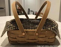 Close view of a Small Oval Basket with khaki check liner folded over edges and attached wooden handles