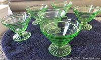 Six green glass custard cups arranged in a loose circle on a towel, showing ribbed pattern, flared tops, and footed bases.