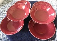Six red ceramic bowls stacked in two piles, each bowl about 6 inches wide at the top, glossy finish.