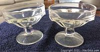 Pair of clear glass custard cups with hexagonal stems shown side by side on dark fabric