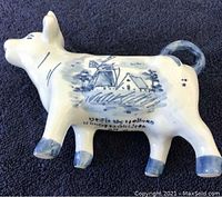 Photo showing side view of Dutch ceramic cow creamer with blue windmill and countryside design, showcasing its cream pitcher opening and tail handle.