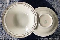 Two cream-colored ceramic serving bowls with gold trim shown from top and bottom side, one displaying maker's mark on base.