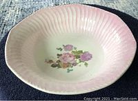 Serving bowl with pink fluted rim and floral pattern in center, displayed on dark fabric background.