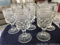 Set of eight antique-style stemware crystal glasses arranged in two rows on a dark cloth, showing detailed diamond and hobnail patterns, clear glass with starburst pattern on base.