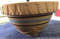 Side view of larger antique crock bowl showing textured rim with cut designs and painted horizontal stripes in blue and brown