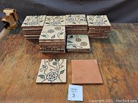 Overview of 56 stacked vintage ceramic tiles with floral pattern on glazed front sides, backs of tiles show terracotta clay.