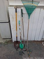 Photo of 9 garden tools including two green plastic leaf rakes, shovels, a garden hoe, and handheld cultivators showing wear.