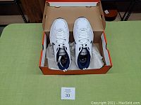 Pair of white Nike Air Monarch IV shoes in open orange Nike box on green surface