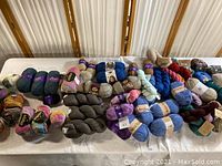 Large assortment of new yarn skeins and balls displayed on a table in various colors and textures, including solid and variegated yarns.