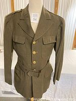 Front view of WWII US Army military coat on mannequin showing five-button closure, lapel collar, chest buttons and belt.