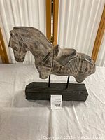 Side view of ceramic horse sculpture showing detailed harness and saddle, mounted on wooden base.