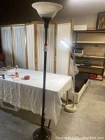 Full view of the tall torch lamp next to a table, showing the entire height and design.