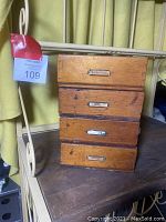 Four-drawer antique wooden box with metal label holders, showing wear and age marks on wood surface.