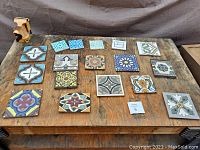 Seventeen vintage fired clay ceramic glazed tiles displayed on wooden surface with varied colors and patterns
