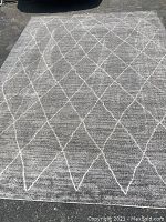 Full view of the large gray area rug laid out on an outdoor surface showing the white diamond trellis pattern.