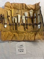 Full view of antique grooming set rolled open on fabric surface showing 11 grooming tools with mother of pearl and other materials handles organized in fabric roll-up case.