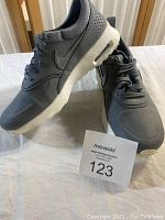 Pair of grey Nike tennis shoes displayed, side and angled view showing design, laces, and sole with air pocket heel