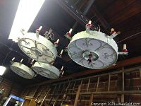 Four round wagon wheel style metal ceiling light fixtures mounted on ceiling, showing white and light green paint with red candle-like light holders evenly spaced around each fixture.