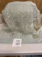 Overview of five cut crystal wine glasses and one small tinted glass set on a cloth background.