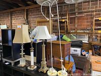 Five lamps shown together; two tall white IKEA spotlight floor lamps and three smaller decorative table lamps on black surface. One table lamp missing shade.